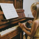 Two young girls playing piano together indoors, focused on a music sheet.